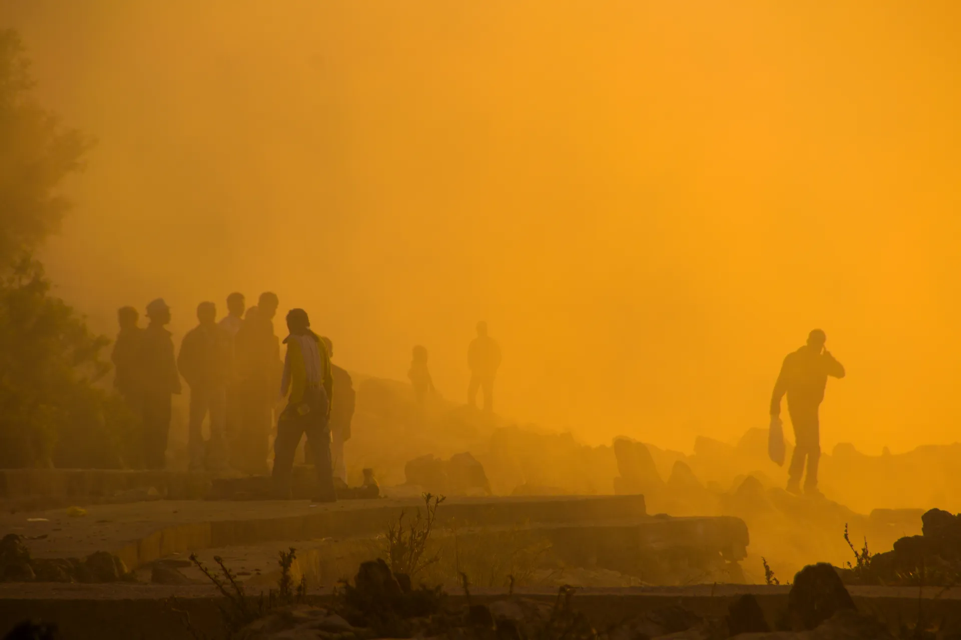 People standing in silhouette on a river bank at sunrise.